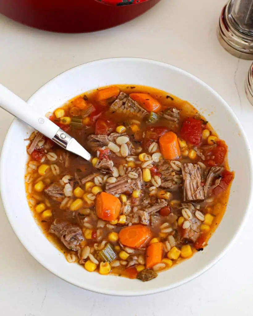 A bowl of beef barley soup with a spoon in it. 