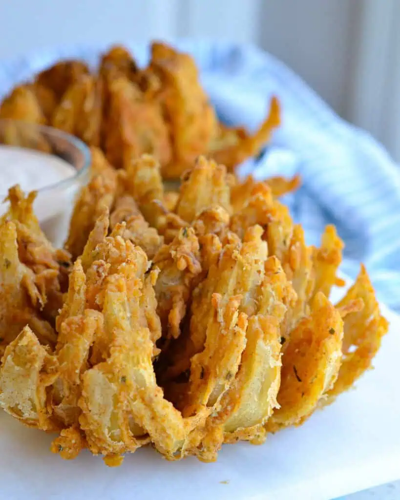 Fried blooming onions on a platter with sauce. 