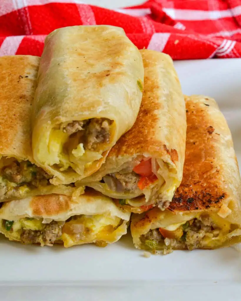 Several breakfast burritos stacked on a plate. 