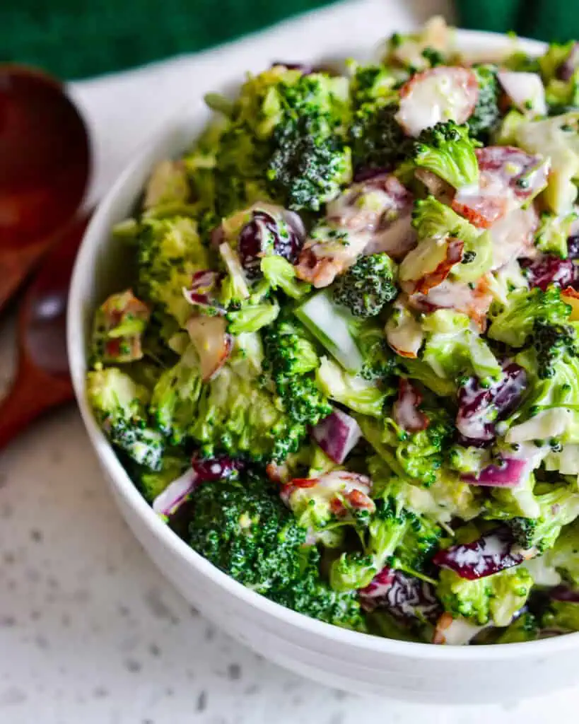 Broccoli salad in a serving bowl with wooden spoons on the side. 