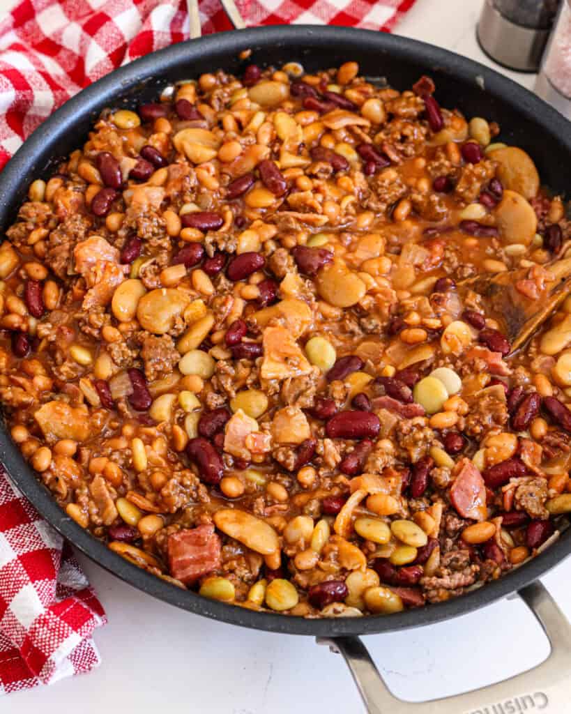 Calico beans in a large skillet with a wooden spoon. 