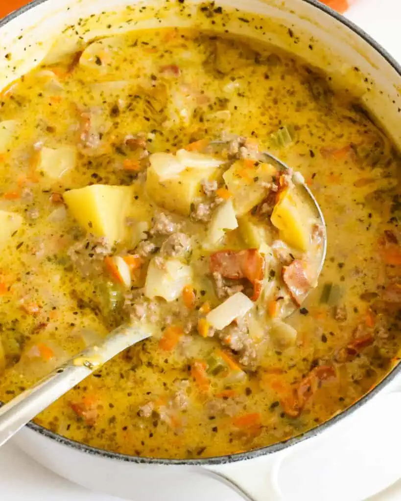 A ladle full of cheeseburger soup in a Dutch oven full of cheeseburger soup. 