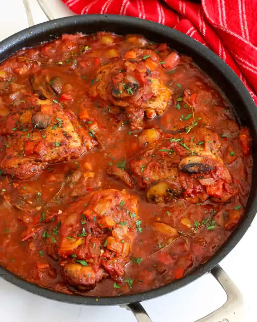 Chicken cacciatore in  a skillet with a towel in the background. 