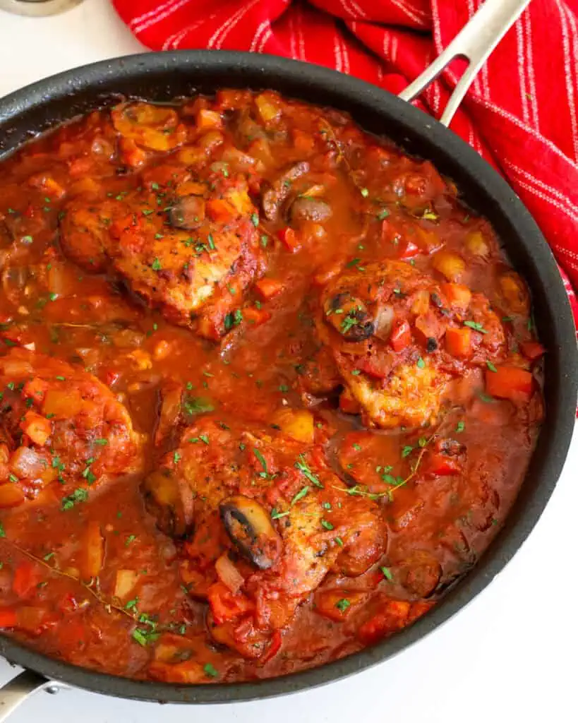 Chicken cacciatore sprinkled with fresh herbs in a large skillet. 