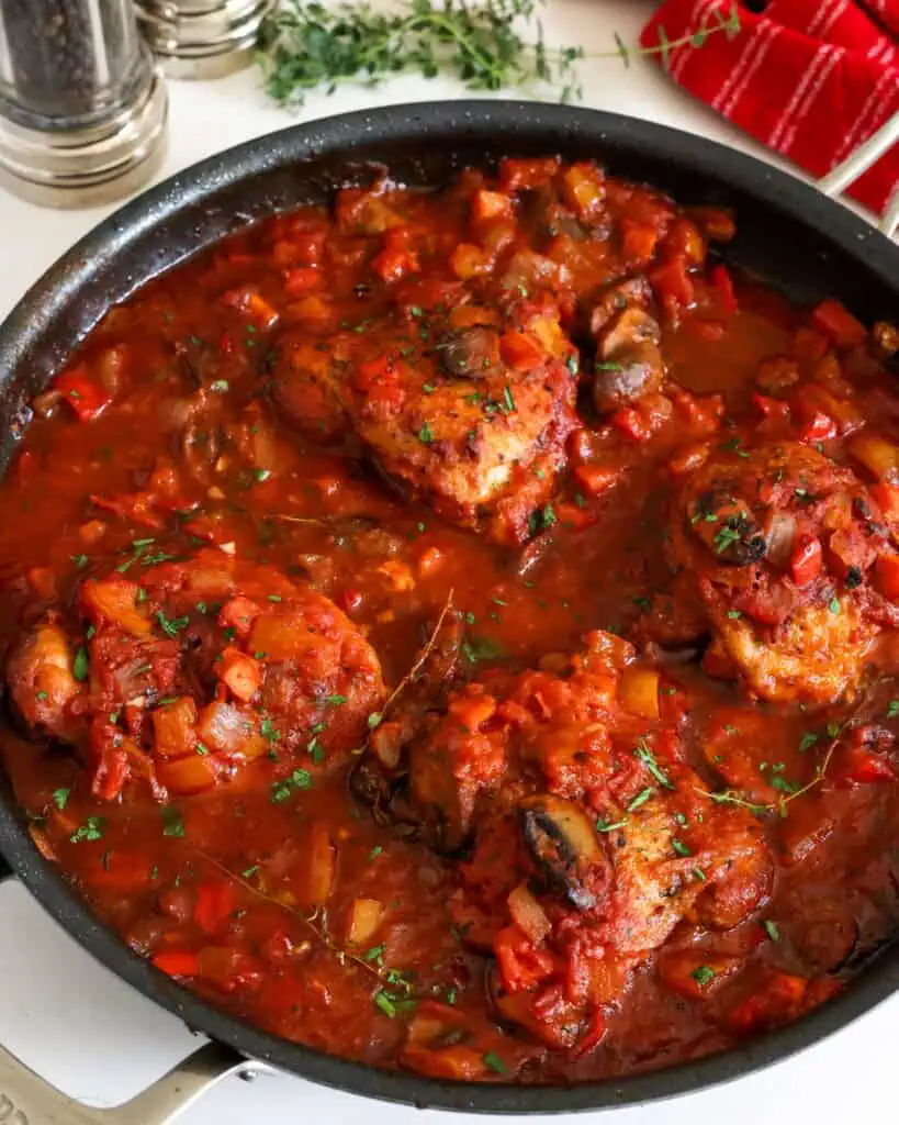 Chicken cacciatore in a large skillet with salt and pepper shakers in the background. 