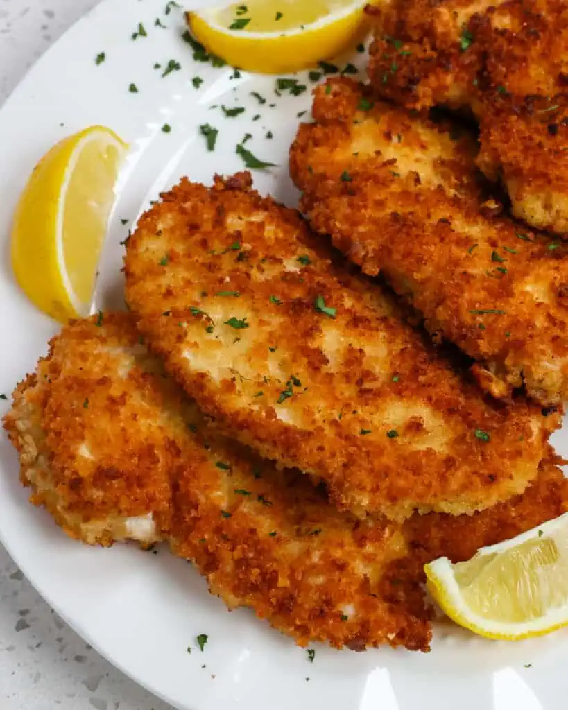 Chicken schnitzel on a plate with fresh lemon wedges. 
