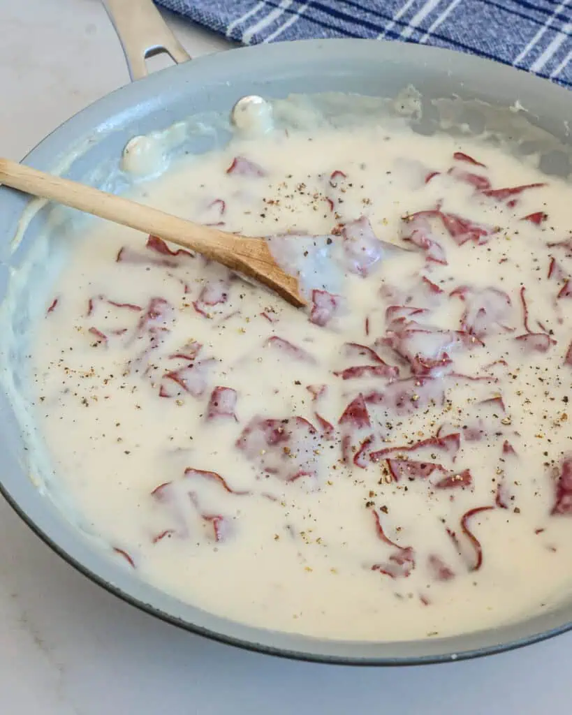 A skillet and a wooden spoon full of creamed chipped beef. 