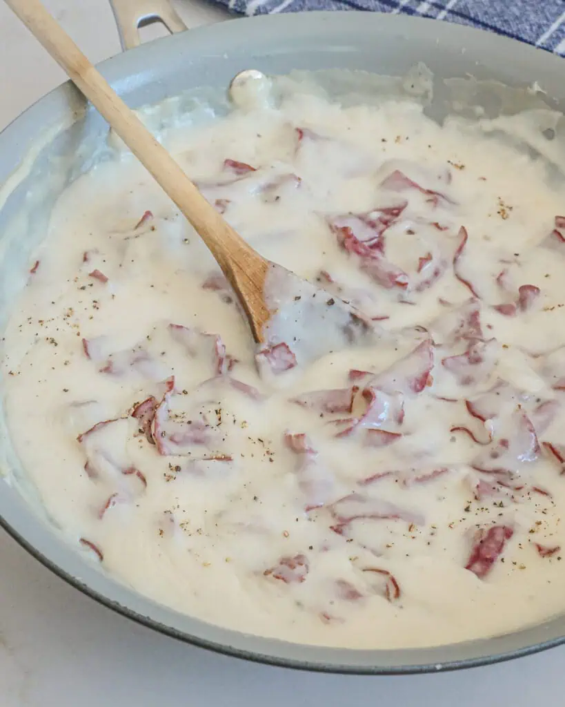 Creamed chipped beef in a skillet with a wooden spoon. 