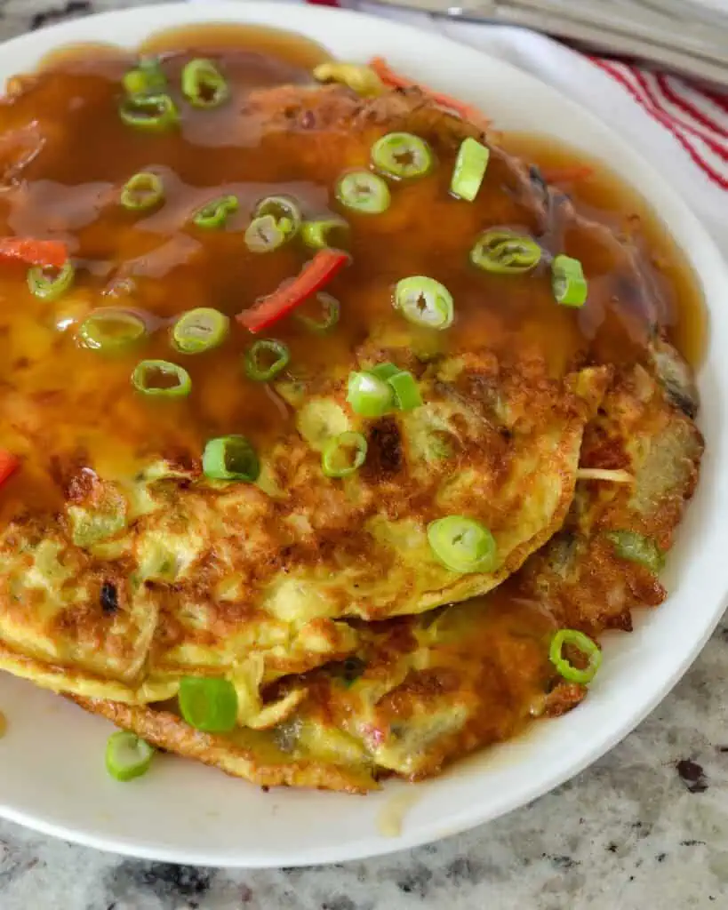 Egg foo young on a plate with gravy and green onions. 