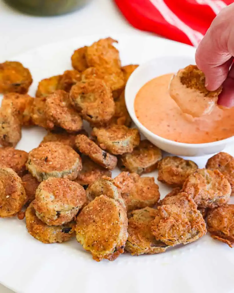 Deep fried crispy pickles on a plate with a bowl of dipping sauce. 