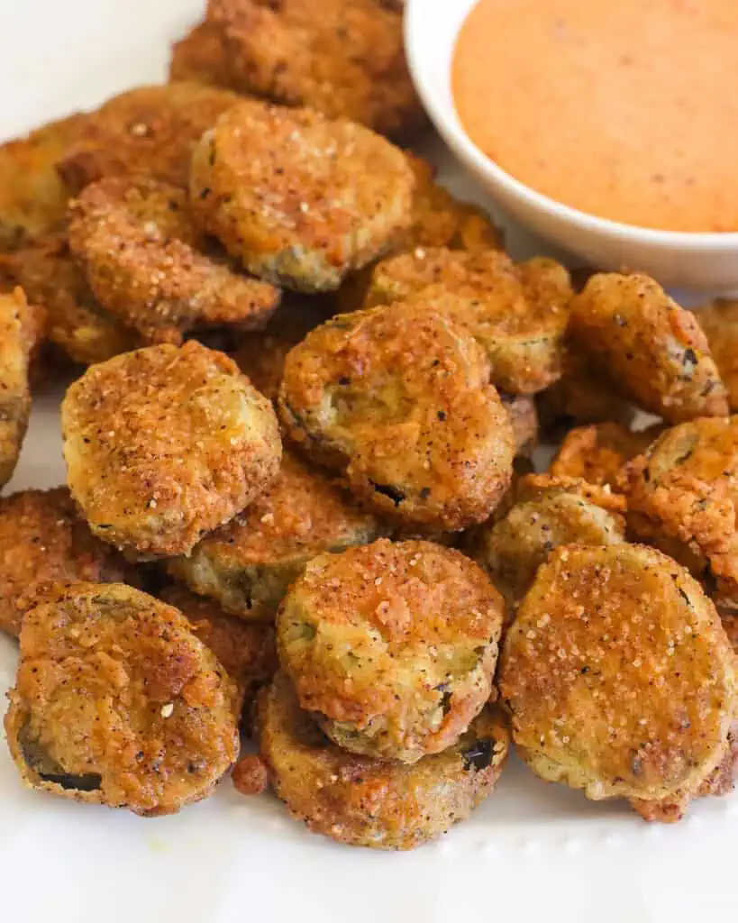 A close up view of fried pickles on a plate with comeback sauce. 