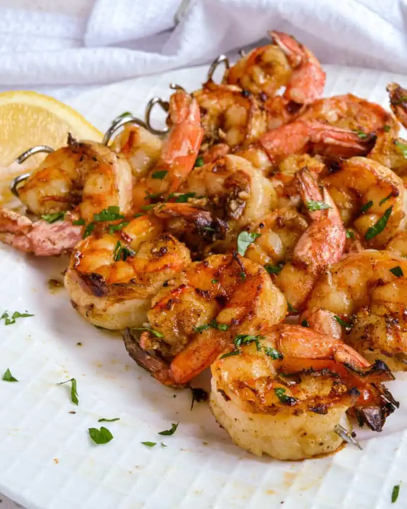 Grilled shrimp on skewers with fresh herbs and lemon wedges. 