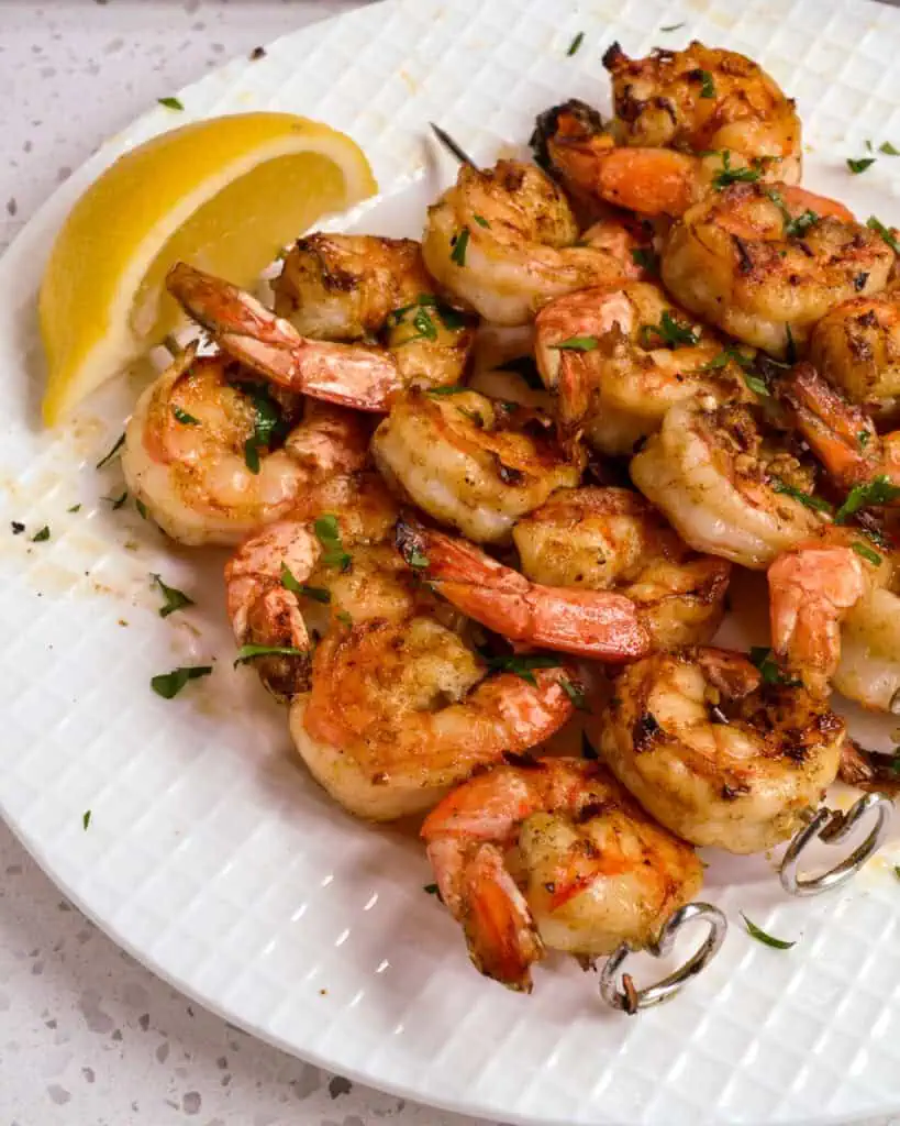 Cooked marinated shrimp on skewers on a serving plate with lemon wedges. 