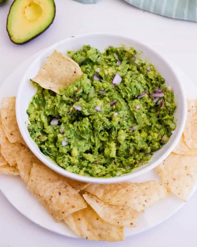 A bowl of guacamolie with tortilla chips on the side and a tortilla chip in the bowl. 