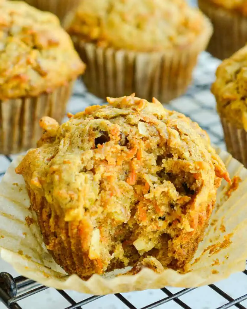 A morning glory muffin with a bite taken out of it on a cooling rack. 