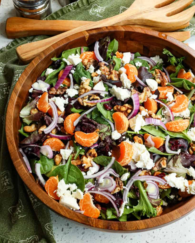 Mandarin orange salad in a wooden bowl with salad tongs and salt and pepepr shaker off to the side. 