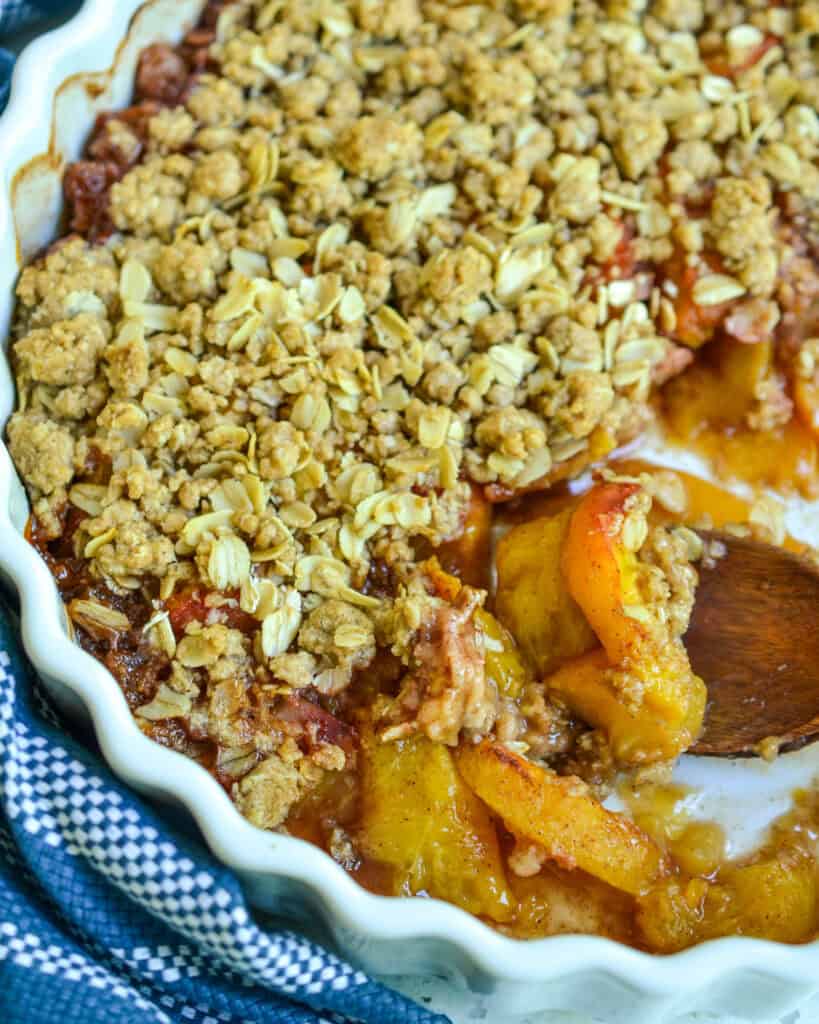 A baking dish with peach crisp and a wooden spoon in it. 