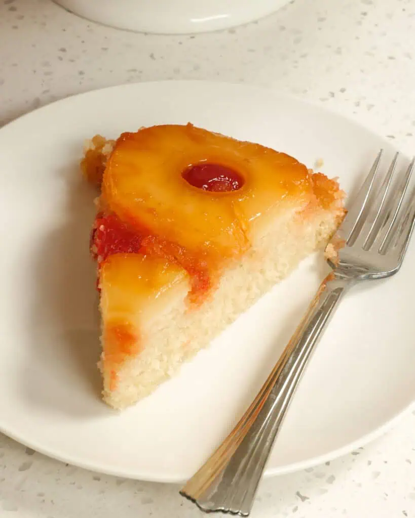 A single slice of pineapple upside down cake on a plate with a fork. 
