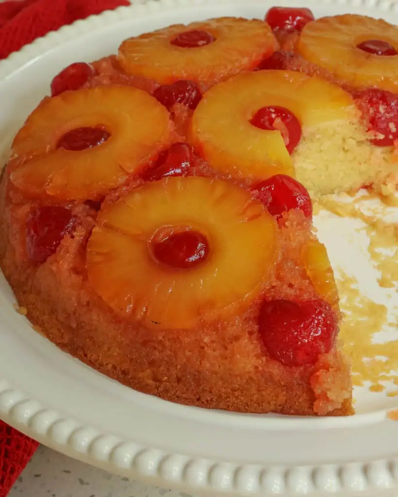 A pineapple upside down cake on a large platter with a couple slices removed. 