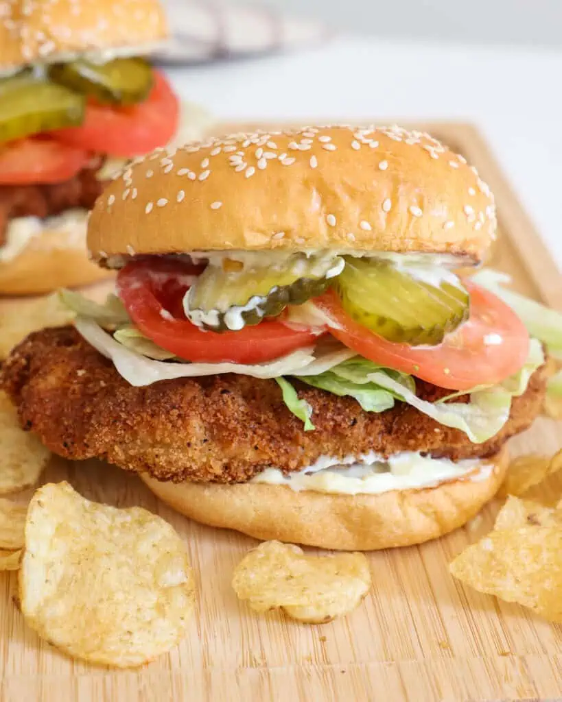 Fried pork tenderloin sandwich on a bun with mayo, lettuce, tomato, and pickle. 