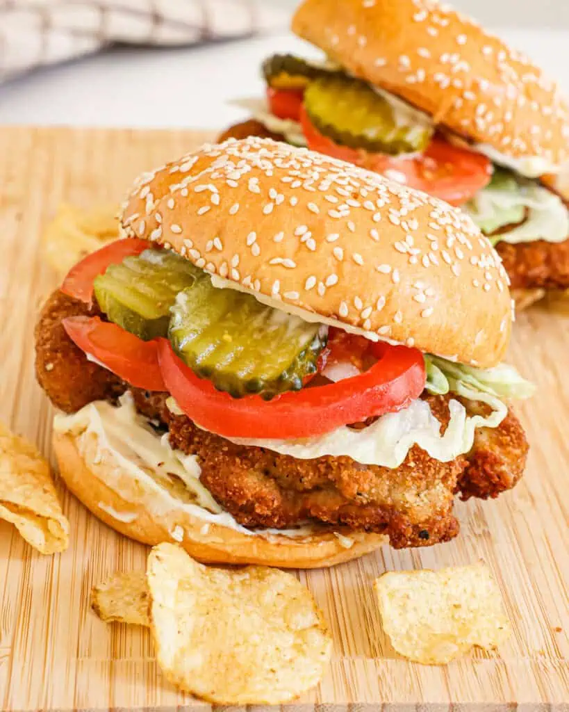 Two fried pork tenderloin tenderloin sandwiches with mayo, lettuce, tomato. and pickle. 