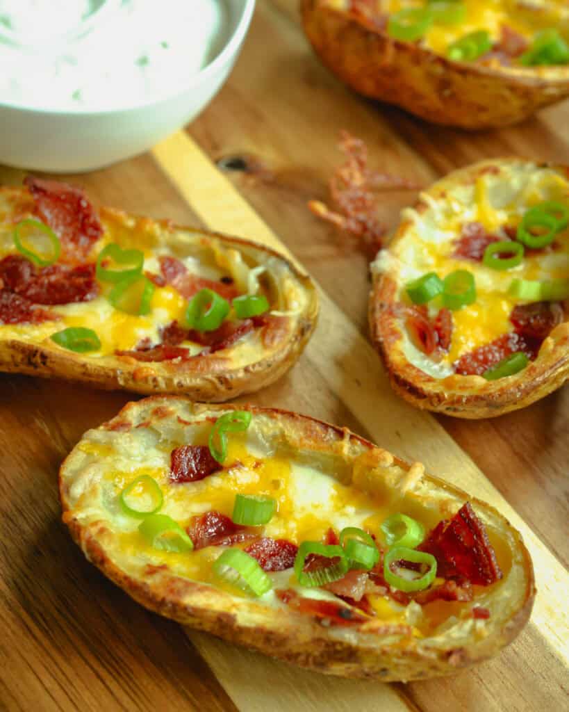 Baked potato skins on a cutting board with a bowl of sour cream. 