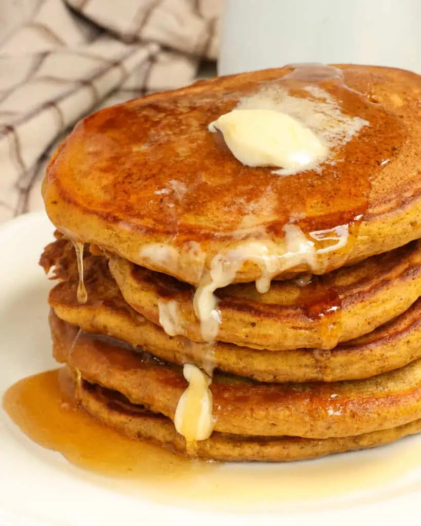A fresh stack of pumpkin pancakes with syrup and butter dripping down them. 