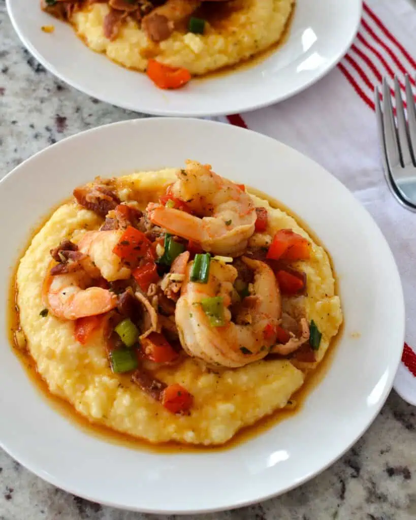 Overhead view of shrimp and grits with bacon, bell peppers, and green onions on a white single serving plate. 