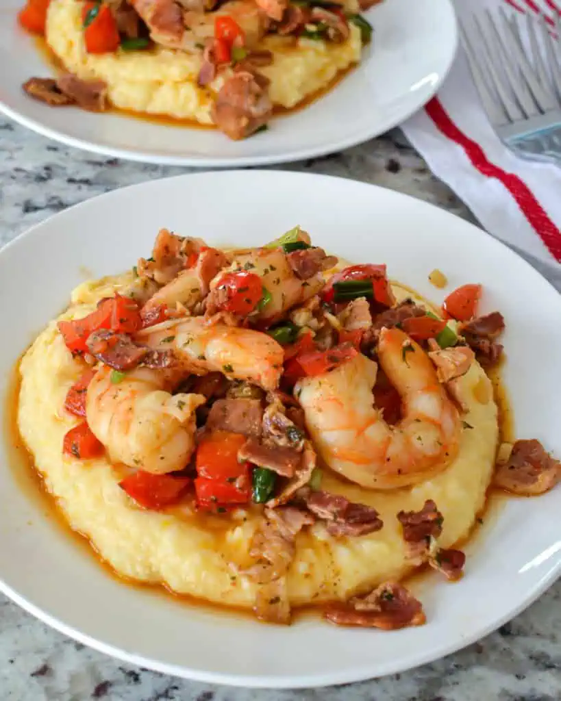 Shrimp and grits on a single serving plate with two forks and a read and white towel in the background. 