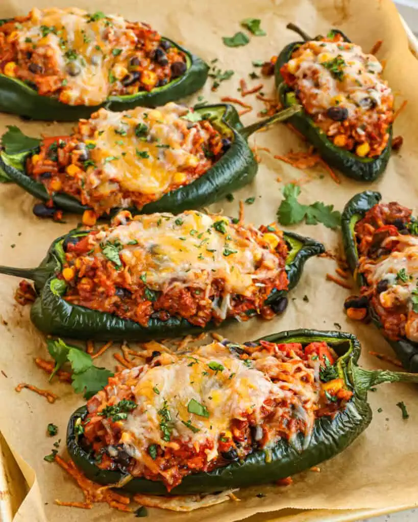 Six baked and stuffed poblano peppers on a baking sheet. 