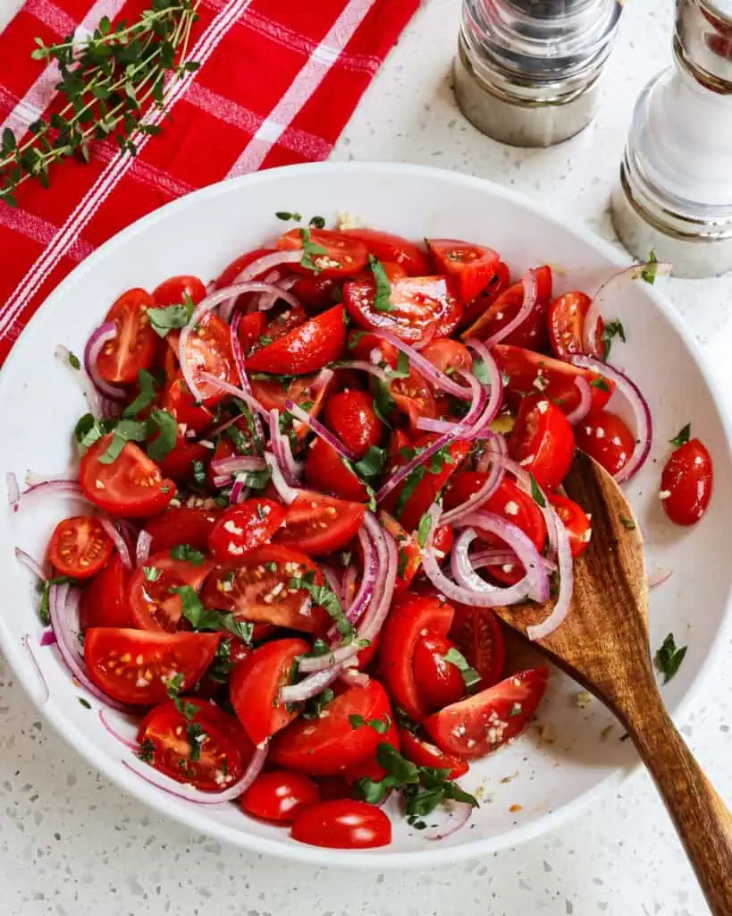 Overhead view of tomato salad in a large bowl with fresh herbs and salt and pepper shakers in the background. 