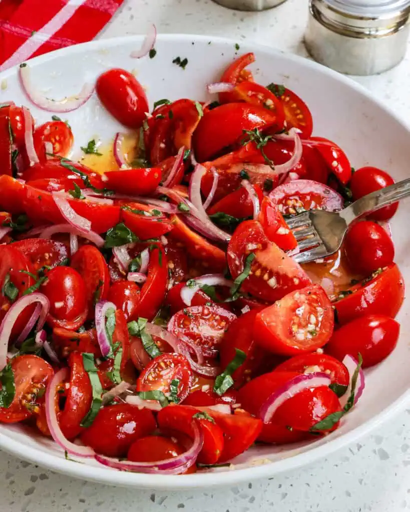 Tomato salad in a bowl with a towel and salt and pepper shaker in the background. 