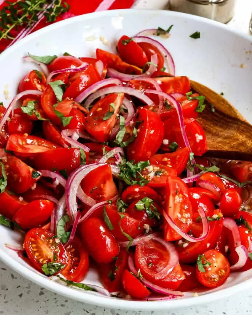 A big bowl of tomato salad with a wooden serving spoon. 