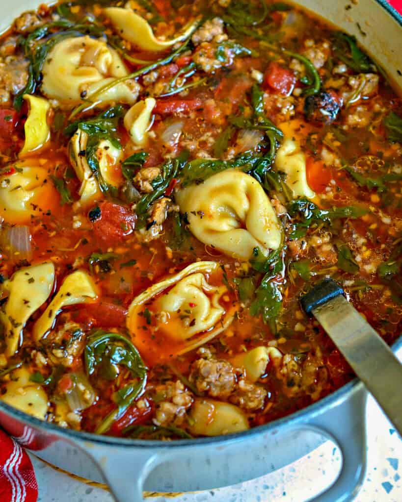 A dutch oven full of cheese tortellini soup with sausage. 