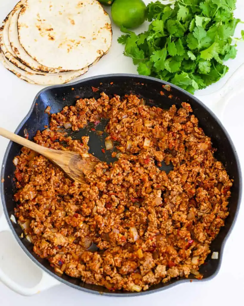 A large skillet full of seasoned ground turkey with fresh cilantro and charred taco shells in the background. 