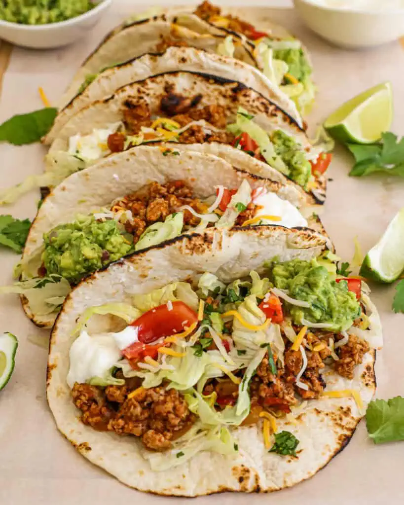 A wooden cutting board with ground turkey tacos with lime slices. 