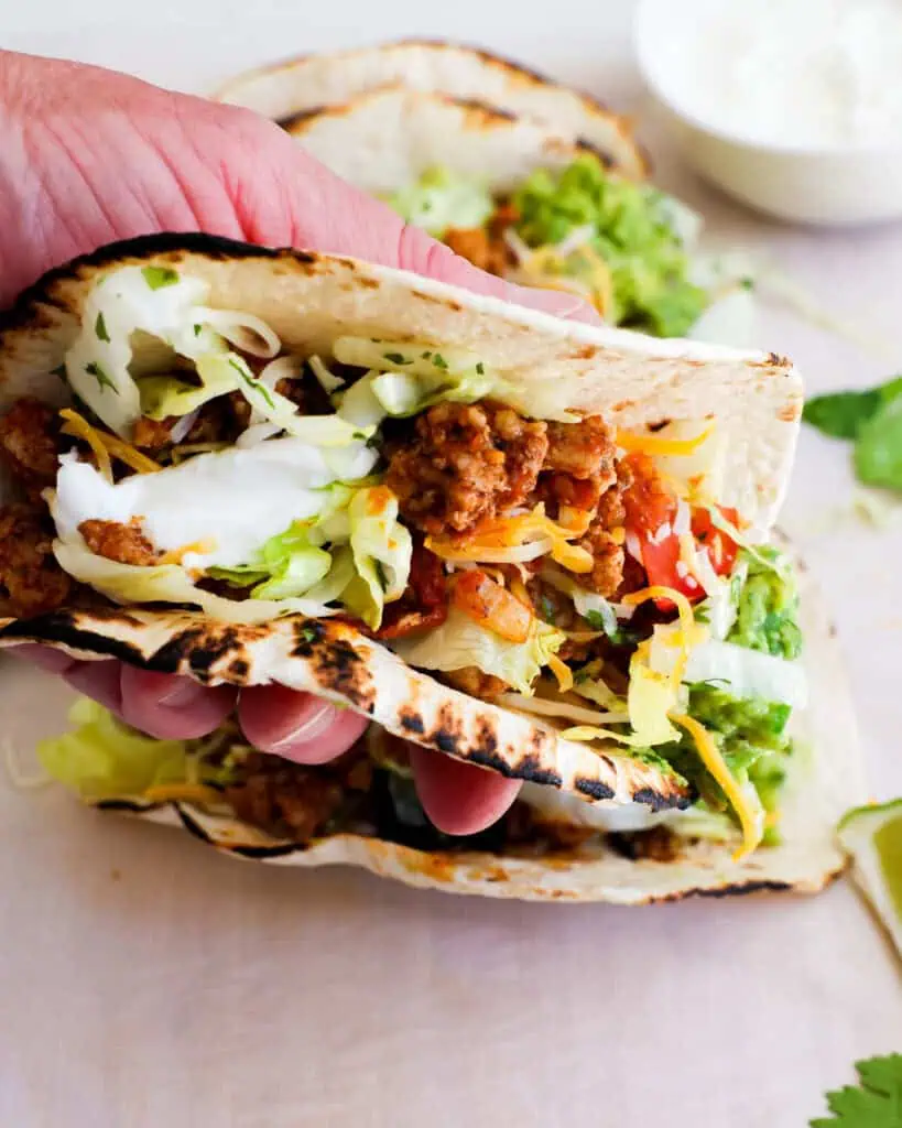 A ground turkey taco with lettuce, tomato, sour cream, and guacamole. 