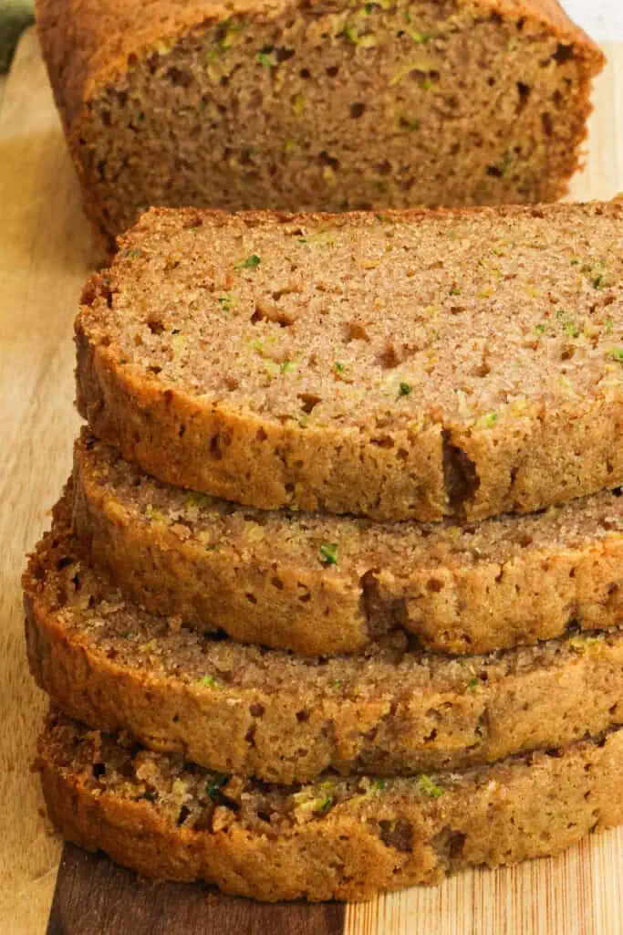 Four pieces of zucchini bread stacked on a wood cutting board. 