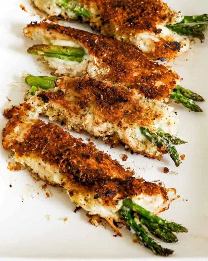 Four browned asparagus stuffed chicken breasts on a platter. 