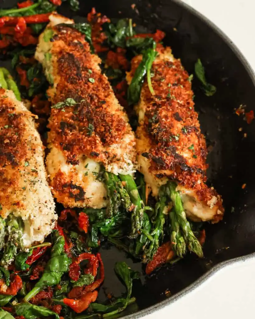 Asparagus stuffed chicken in a skillet with spinach and sundried tomatoes. 