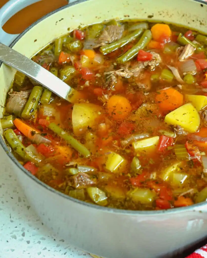 A Dutch oven full of beef vegetable soup with a large ladle in it. 