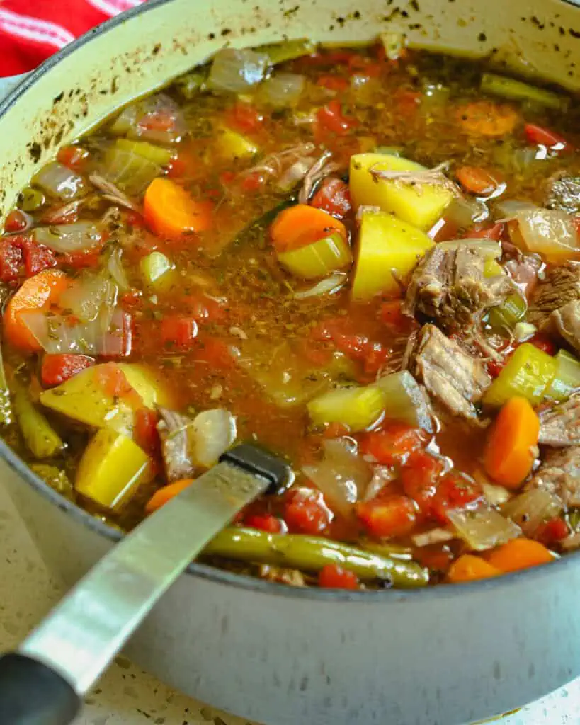 A large pot of beef vegetable soup with a ladle in it. 