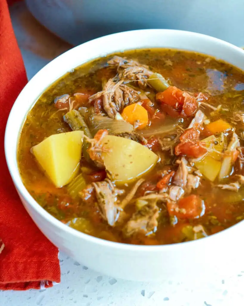 A close up view of beef vegetable soup with tender chunks of slowly simmered chuck roast, onions, celery, carrots, potatoes, tomatoes, and green beans.