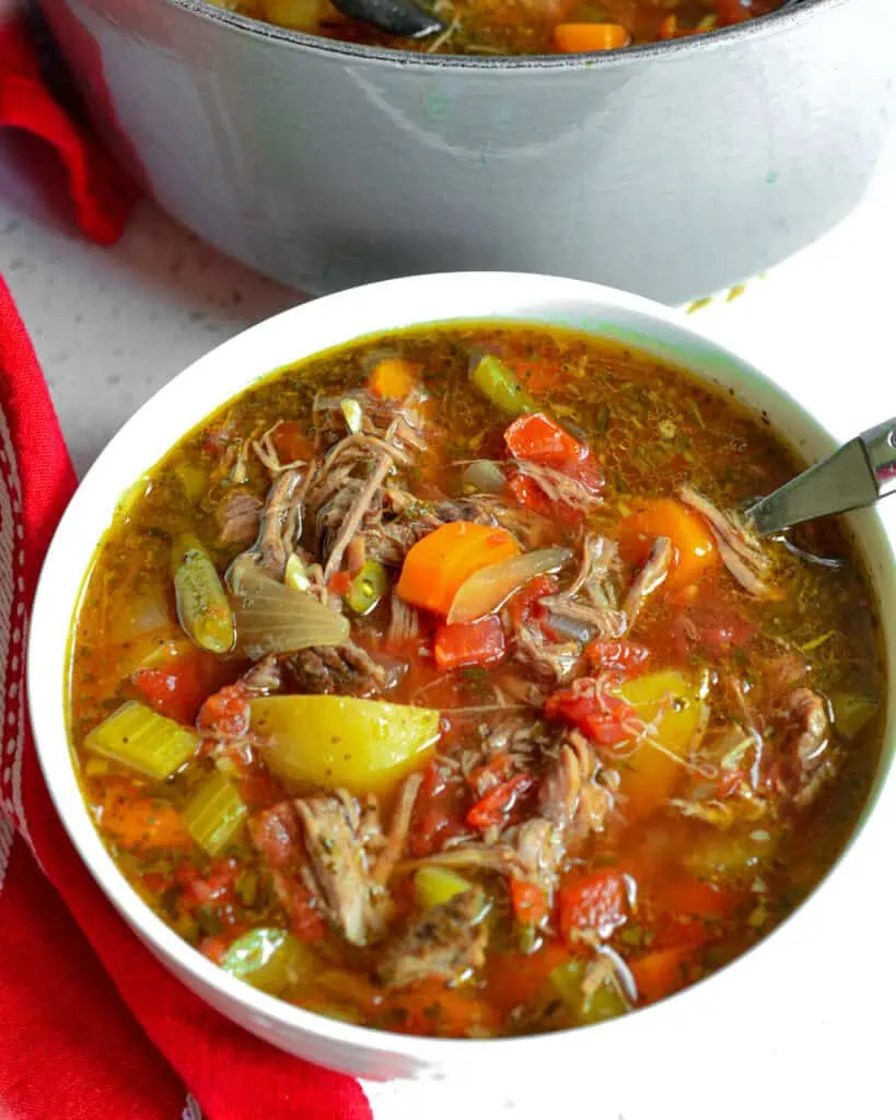 A bowl full of beef vegetable soup withe a spoon in it. 