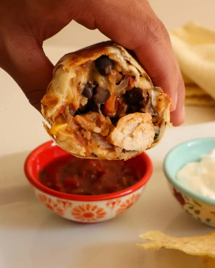 The inside of a chicken burrito over a bowl of salsa and a bowl of sour cream. 