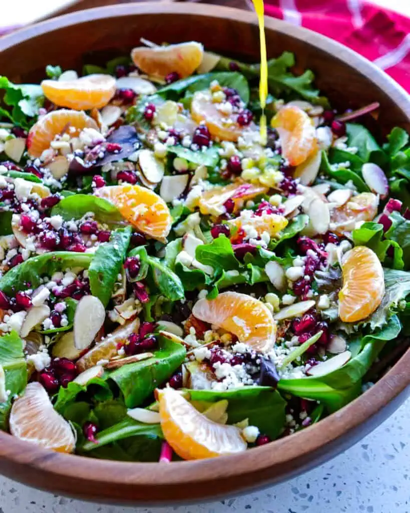 Christams salad in a wooden bowl with honey mustard vinaigrette drizzled over it. 