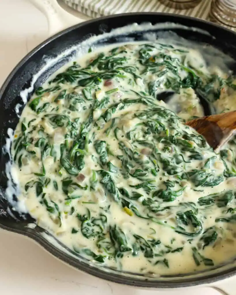 Creamed spinach and a wooden spoon in a large skillet. 