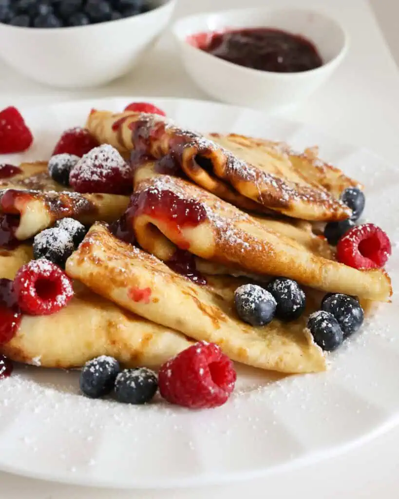 Layered crepes on a plate with raspberry jam and powdered sugar. 