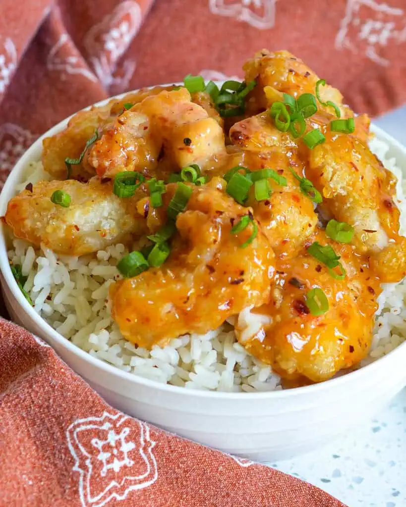 Bang bang shrimp in a bowl with rice and chopped scallions. 