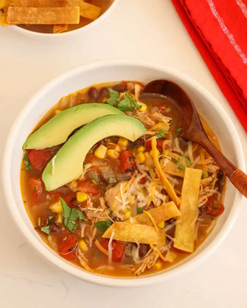 Crock pot chicken tortilla soup in a bowl with cheese, cilantro avocado slices. and fried corn tortilla strips. 